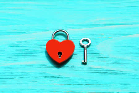Red heart-shaped padlock and silver-toned skeleton key on a blue wooden background with copy space. Strong romantic relationships concept.の写真素材