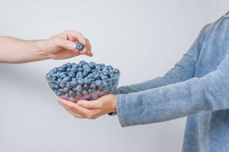 Hand taking a blueberry from a large glass bowl held by a woman wearing a color matching sweatshirt.の写真素材