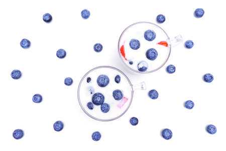 Two cups of blueberries yogurt desserts with scattered berries on white.の写真素材