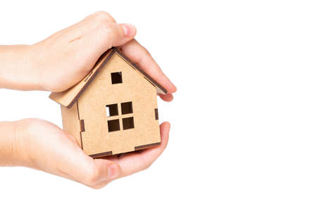 Holding a miniature wooden house model with both hands isolated on neutral background. Home insurance and care concept.の写真素材