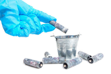 Gloved hand throws a heavily corroded dead battery in a small steel bucket isolated on white. Toxic waste disposal concept.の写真素材