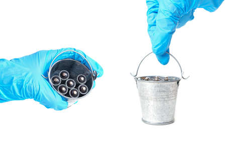 Glove hand holding a small steel bucket full of heavily corroded used AA type batteries on white.の写真素材