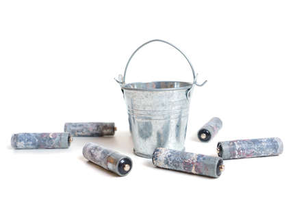 Heavily corroded AA type batteries scattered by a small steel bucket isolated on white. Toxic waste disposal concept.の写真素材