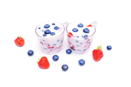 Two cups of fresh berry yogurt desserts with whole strawberries and blueberries isolated on white background.の写真素材