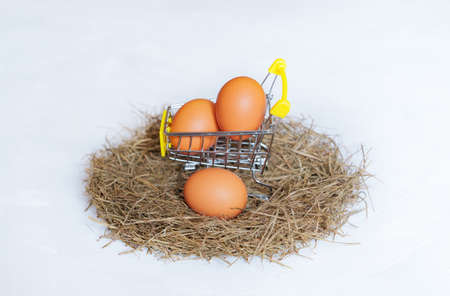 Miniature shopping cart with chicken eggs placed in a hay nest isolated on neutral background. Farm-to-table concept.の写真素材
