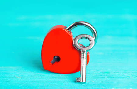 Small red heart-shaped padlock with a silver-toned master key on a blue wooden background. Symbolic romantic concept.の写真素材
