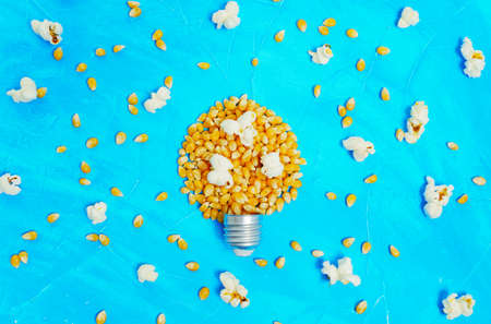 Unpopped and popped corns scattered on blue, some kernels arranged into a lightbulb shape.
