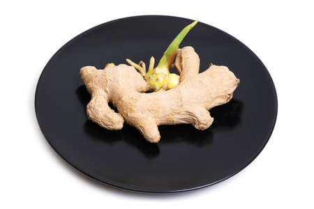 Close-up of a sprouted ginger root on a black plate isolated on white
