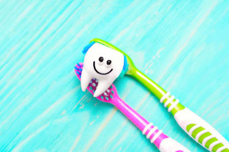 Cute smiling tooth character and two vivid toothbrushes isolated on a blue wooden background, selective focus.の写真素材