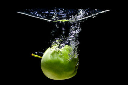 Green apple going underwater with splashes and bubbles on black background.の写真素材