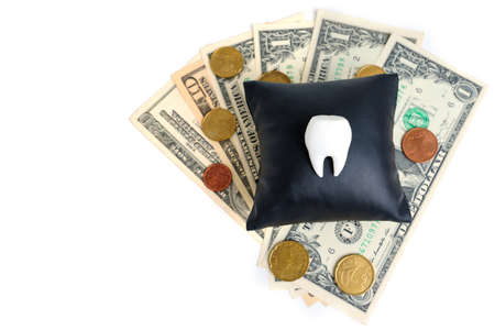 White tooth on a black leather pillow with some dollar bills and euro coins underneath isolated on white.の写真素材