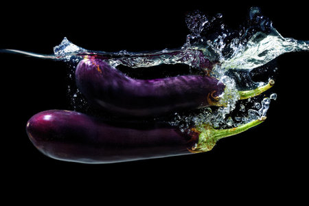 Two whole eggplants dropped in water with splashes on blackの写真素材