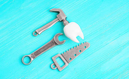 Human tooth model, steel hammer, wrench and handsaw on a blue wooden background with copy space. Choosing a good dentist.の写真素材