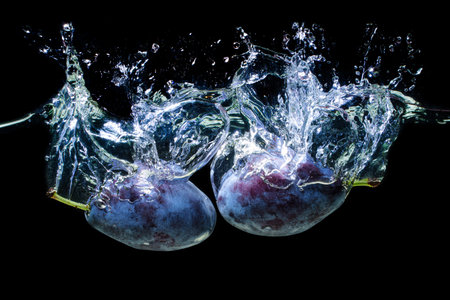 Two damson plums dropped in water with splashes isolated on black background.の写真素材