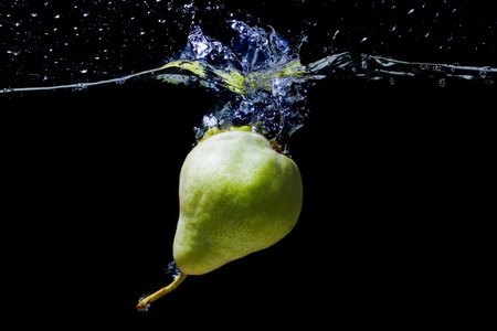 Whole green pear dropped in water with splashes isolated on black background.の写真素材