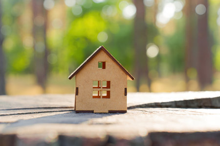 Close-up of a wooden toy house model placed on a tree stump in a forest area. Nature and real estate concept.の写真素材