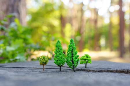 Toy trees grow on a trees stump against a real autumn forest background.の写真素材