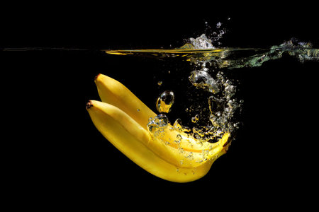 Two ripe yellow bananas dropped in water isolated on black backgroundの写真素材