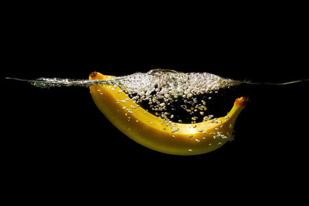 Ripe banana dropped in water with bubbles isolated on black background.の写真素材