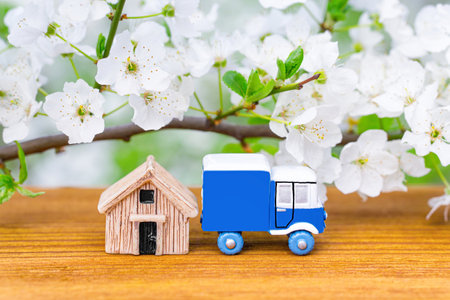Toy truck and small wooden house against a blooming tree background. Spring season home purchase and...