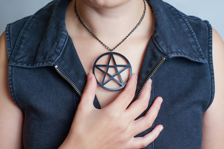 Woman in black denim dress wearing a large pentagram necklace isolate on gray.の写真素材