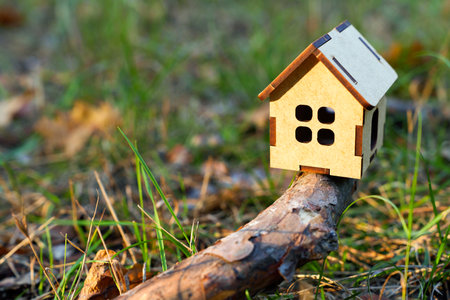 Small toy house placed on a tree branch lying on the ground in the woodsの写真素材
