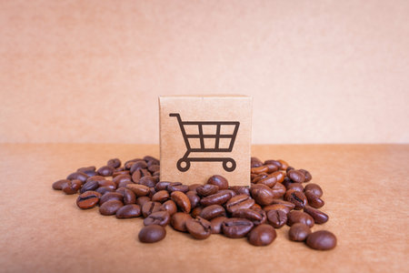 Tiny cardboard box with a shopping cart icon placed on top of a pile of roasted coffee beans isolated on a craft paper background. Coffee blending and supply concept.の写真素材