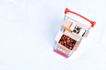 Roasted coffee beans and coffee cups in tiny shipping boxes loaded in a miniature push cart isolated on a neutral background with copy space.の写真素材