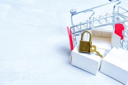 Overturned miniature shopping trolley with delivery boxes and keyed padlock. Online shopping and privacy concept.の写真素材