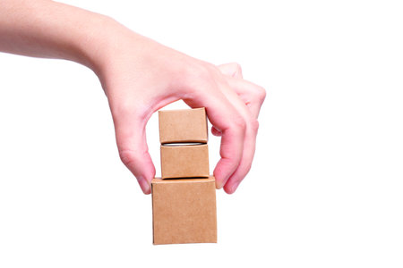 Hand pinch holding a bunch of tiny brown paper shipping boxes isolated on white background. Delivery...
