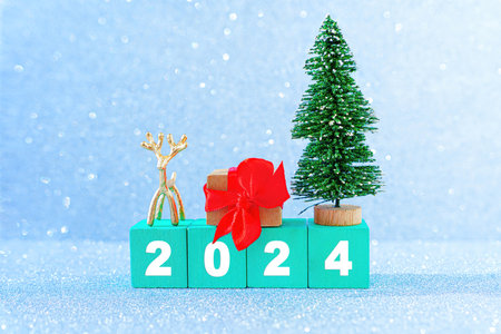 New year 2024 background made from green wooden letter blocks, toy christmas tree, tiny deer figurine and decorated gift box against a glittering background imitating snowing.の写真素材