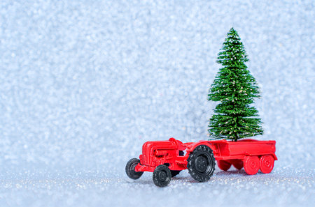 Toy red tractor with a miniature Christmas tree placed in the carriage isolated on a sparkling background. New year trees farming and delivery.の写真素材