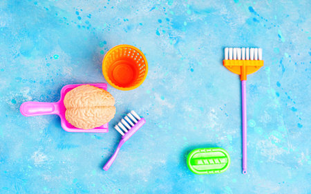 Toy human brain and essential home cleaning tools arranged on blue background. Creative mind...