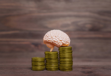 Miniature copy of a human brain placed on top of three coins stacks against a wooden background. Creative business related concept.の写真素材