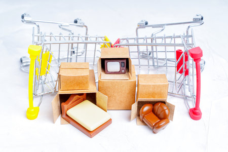 Unpacked tiny delivery boxes with miniature furniture figurines by small push trolleys isolated on...