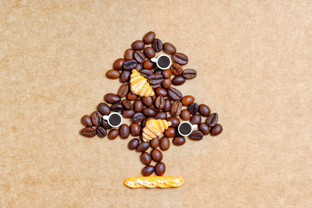 Roasted coffee beans, tiny coffee cups and toy croissants arranged into a Christmas tree shape on a craft paper background.の写真素材