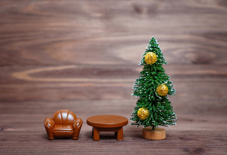 Miniature armchair and table placed by a toy Christmas tree against a wooden background. Getting ready for the New Year night.の写真素材