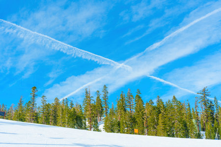 Winter landscape: X-shaped condensation trail in the blue sky above a snowy pine forest on a mountain ski slope. Sense of speed, energy and adventure.の写真素材