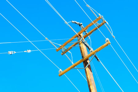 Low-angle view of a wooden power pole and wires against a clear sky, highlighting the details of the power supply infrastructure. Modern and industrial background related technology and engineering.の写真素材