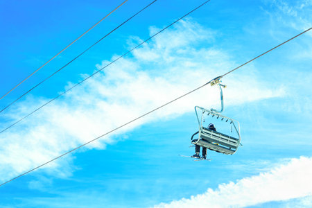 Skier riding a chairlift against a vibrant blue sky. Winter sports, travel and tourism related background.の写真素材