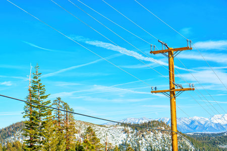 Wooden power pole with wires against a backdrop of mountains and a clear blue sky. Reliable electricity supply in remote areas.の写真素材