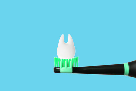 Large tooth model placed on top of a black electrical toothbrush with green bristles isolated on blue background with copy space.の写真素材
