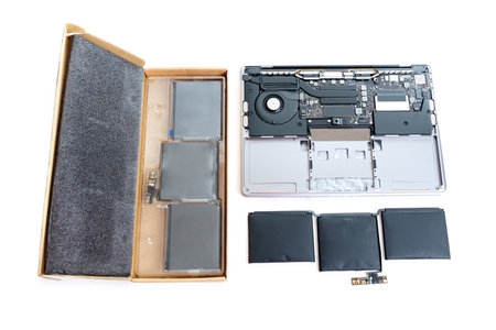 Disassembled laptop with a swollen battery removed, alongside a brand new replacement battery still...