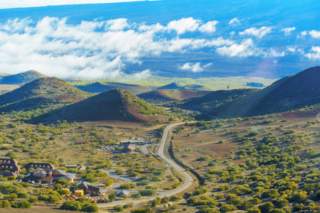 Visitors area in the midst of Mauna Kea's valley with winding road, volcanic hills and clouds seen from the distance.の写真素材