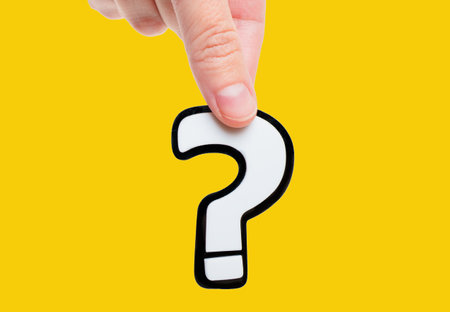 Close-up of a female hand holding a large white question mark symbol, isolated on a plain yellow background. Curiosity, inquiry, exploration or learning concept.の写真素材