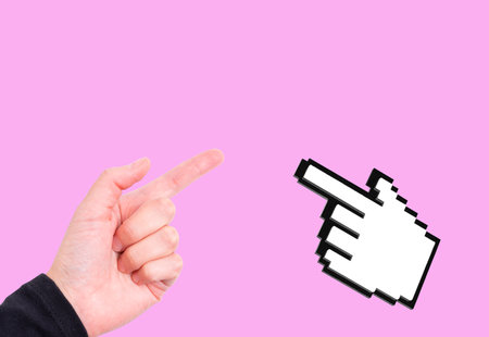 Human hand with pointing finger gesturing and blocky computer mouse hand cursor isolated on pink background with copy space.の写真素材