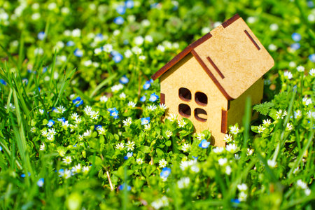 Tiny wooden house model nestled among a vibrant field of colorful flowers and lush greenery.の写真素材