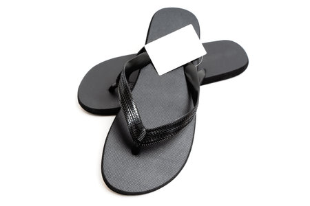 Close-up of a pair of black flip-flops with a blank price tag isolated on white background.の写真素材