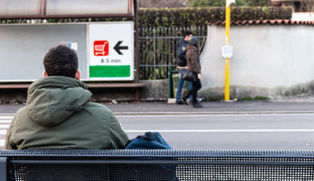 man from behind sitting on a bench looking at the streetの写真素材
