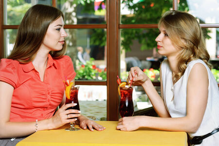 Two girls talking at a cafe table. Girls drink cherry juice sitting by the windowの写真素材